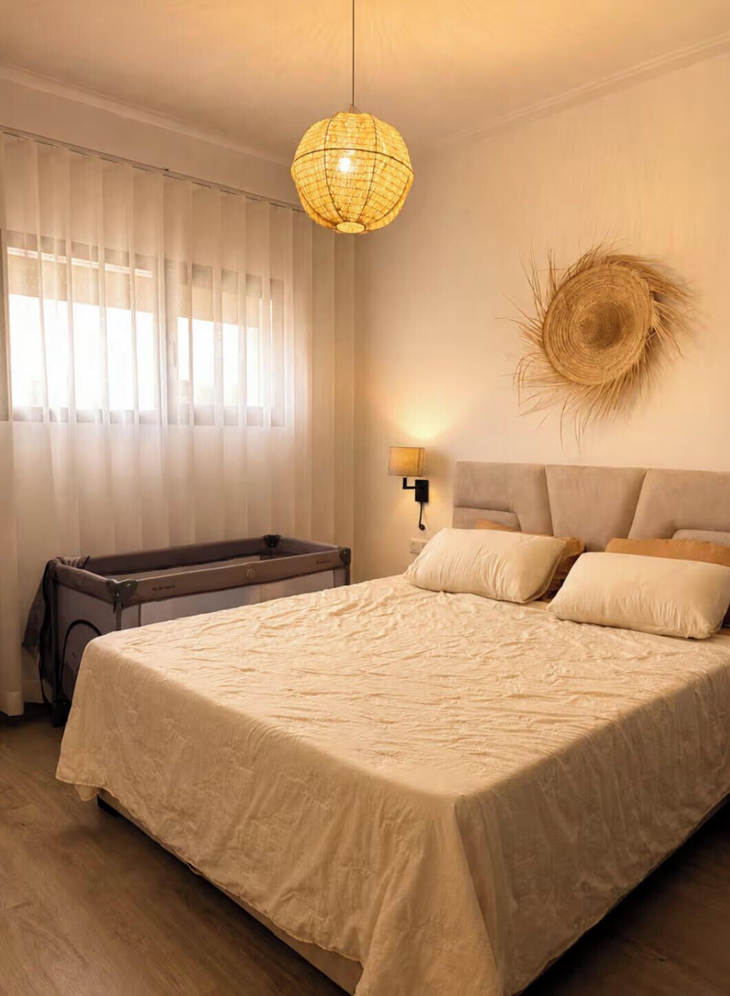 Une chambre à coucher avec un lit, une lampe de chevet, un objet décoratif fixé au mur et une fenêtre avec des rideaux légers.