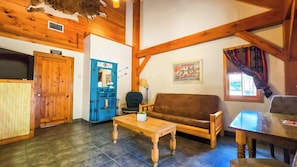 A rustic interior with a wooden ceiling, a blue cabinet, a brown sofa, a wooden table, and a window with curtains. - Sweetwater Gruene Cottages (New Braunfels)