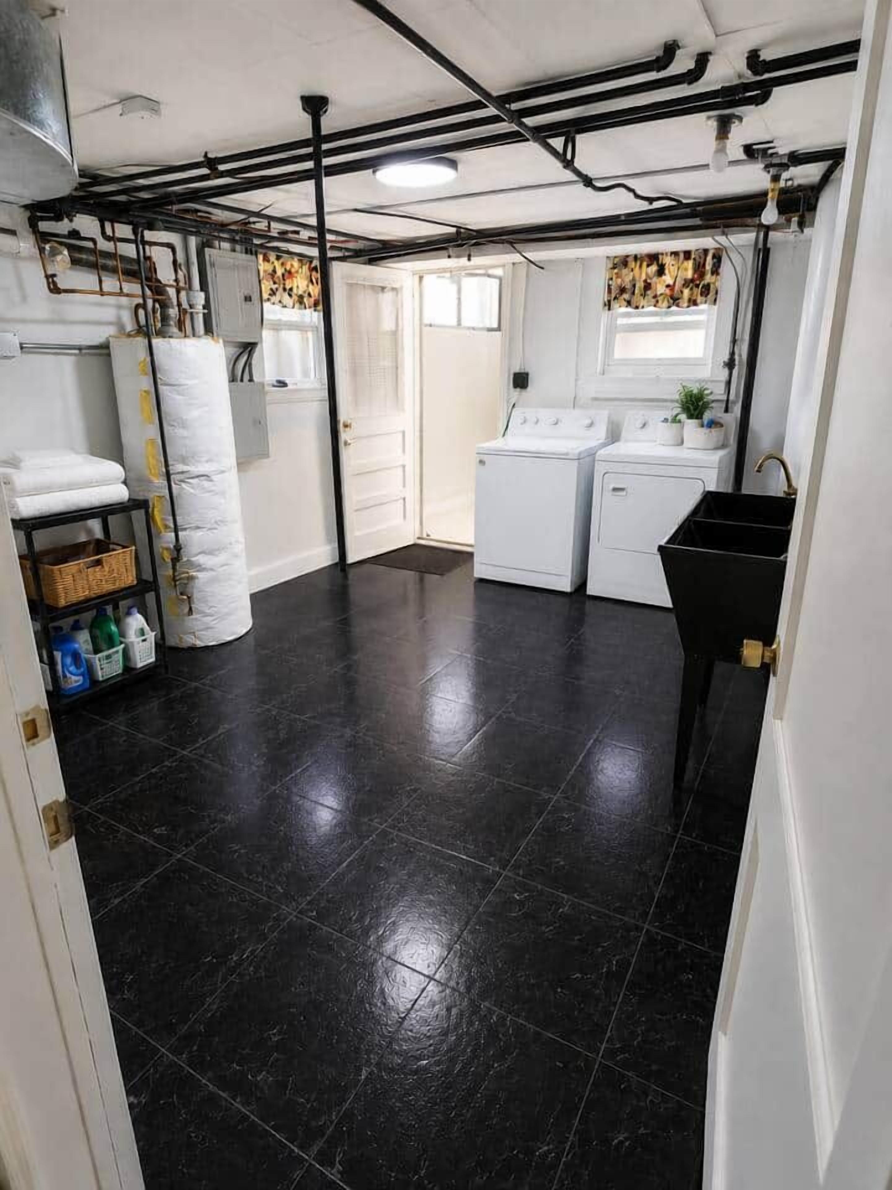 A laundry room with a black tiled floor, a washing machine, a dryer, and a sink.