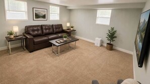 A living room with a brown leather sofa, a glass coffee table, and two side tables with lamps and plants.