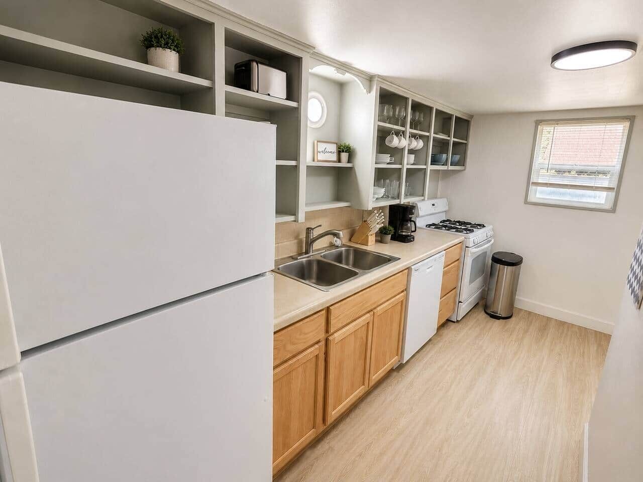 A compact kitchen with white cabinetry, a double sink, a stove, and a trash can.