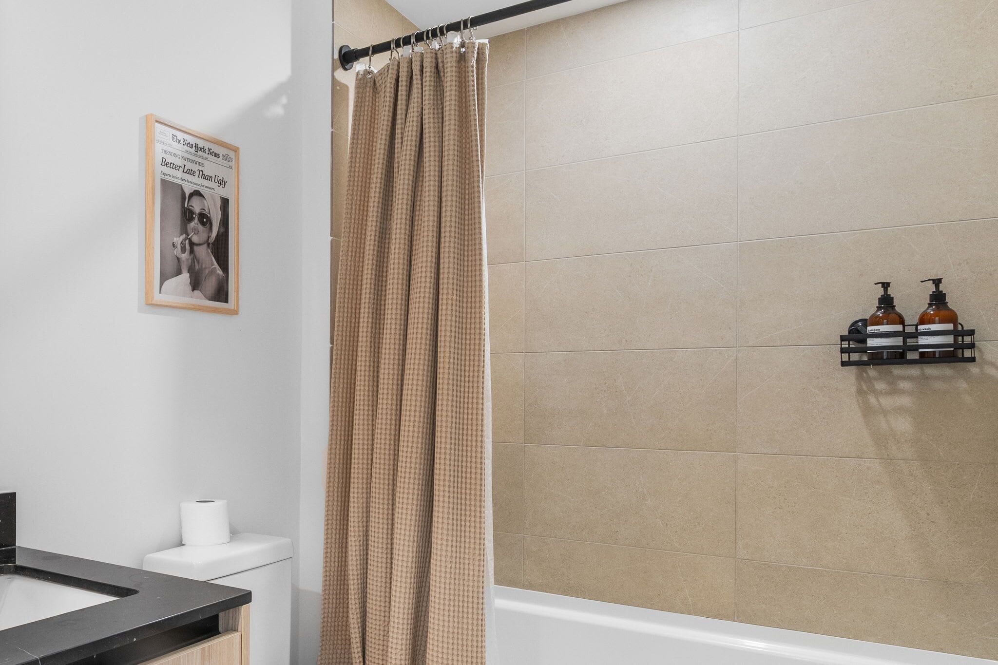 A bathroom with a shower curtain, a toilet, a sink, and a framed newspaper on the wall.