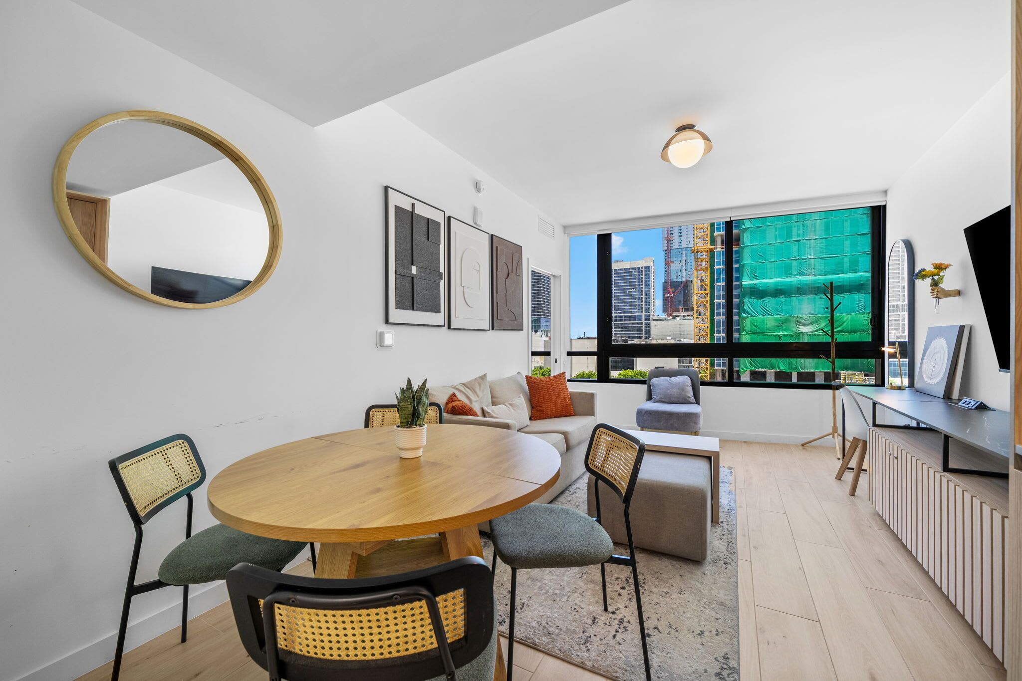 Ein modernes Wohnzimmer mit einem runden Holztisch, einer Couch und einem großen Fenster mit Blick auf Gebäude.