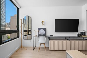 Ein modernes Zimmer mit großem Fenster, Schreibtisch mit Stuhl, Wand-TV und einem dekorativen Spiegel.