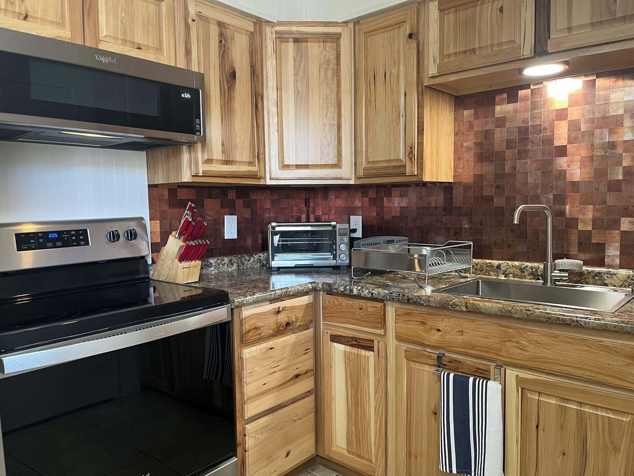 A modern kitchen with wooden cabinets, a stainless steel range hood, a built-in oven, a toaster, and a granite countertop.