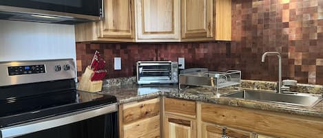 A modern kitchen with wooden cabinets, a stainless steel range hood, a built-in oven, a toaster, and a granite countertop.