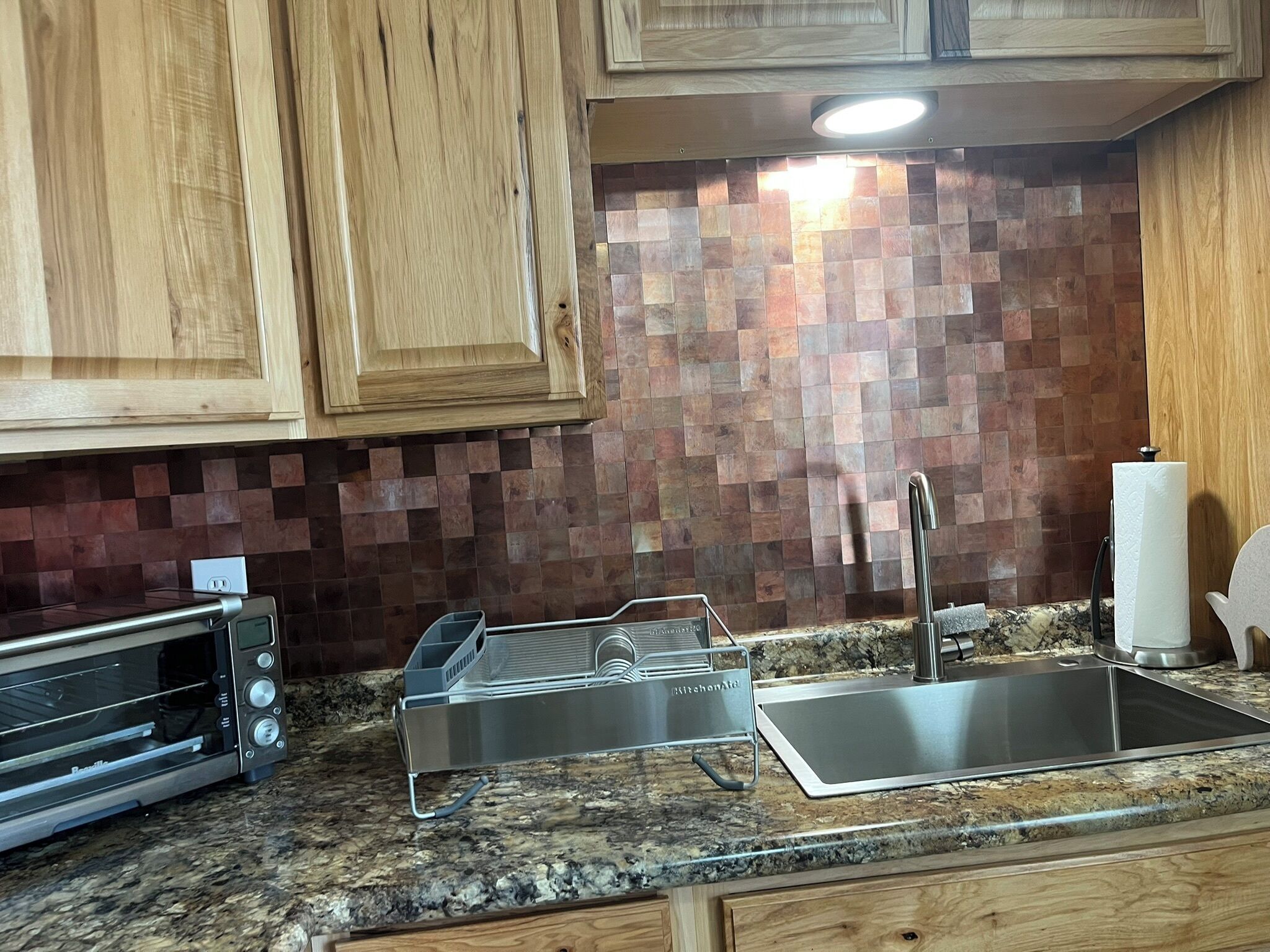 A kitchen with wooden cabinets, a tiled backsplash, a stainless steel sink, a dish rack, and a built-in oven.