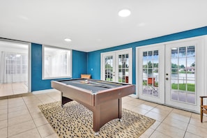 A pool table in a room with blue walls, white doors, and a view of a lake. - Large 3-bedroom house lake view Pembroke Pines, Miami (Pembroke Pines)