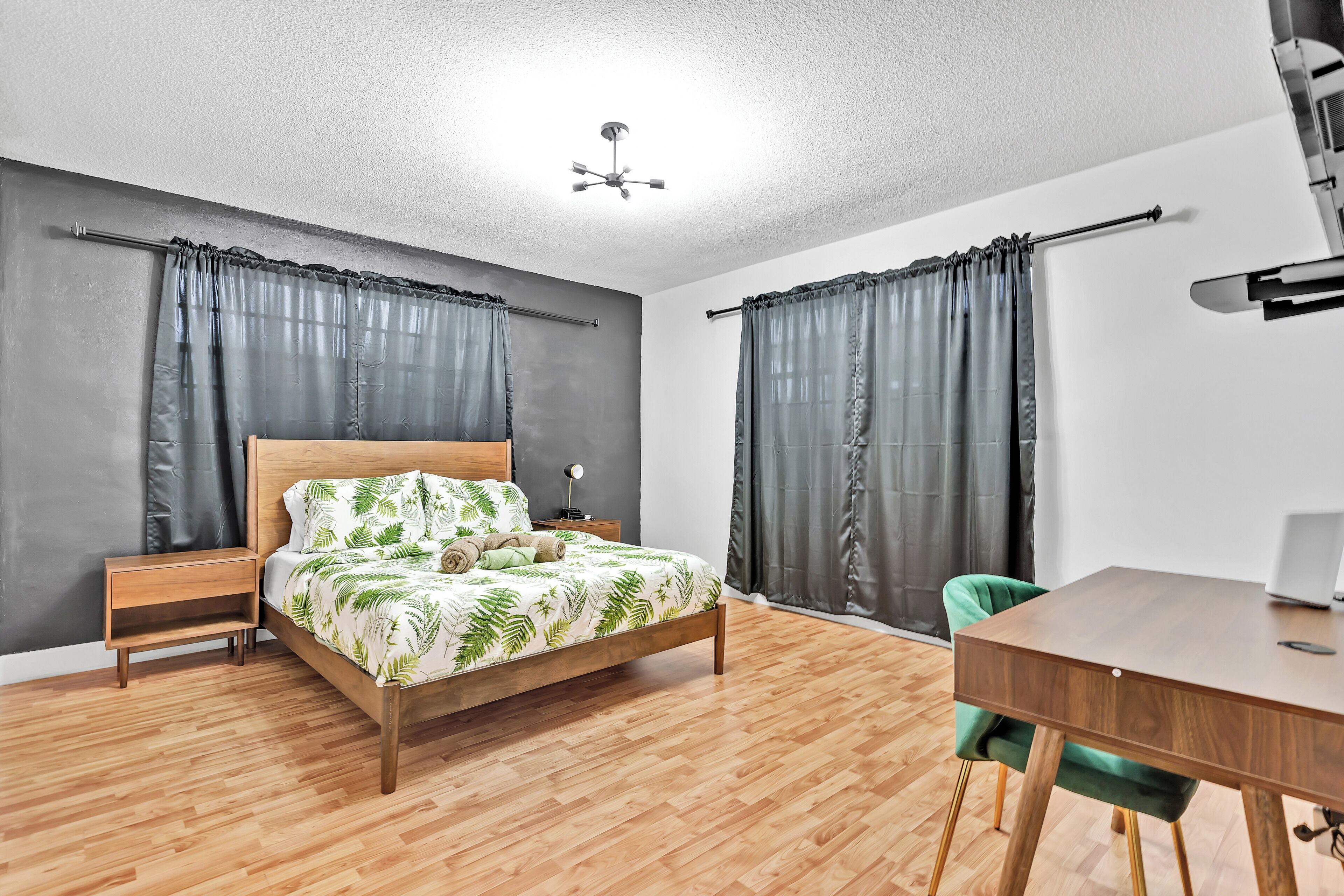A bedroom with a wooden bed, a nightstand, a desk with a chair, and a ceiling fan.