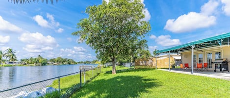 A grassy area with a tree, a fence, and a building with outdoor seating.