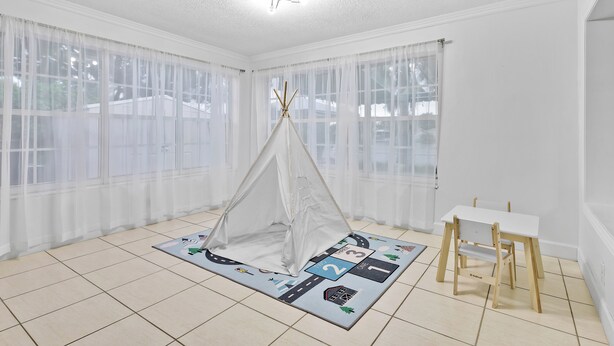 Ein Zimmer mit weißer Decke, einem weißen Tisch und einem Zelt, das auf einer Matte mit Straßen- und Hausmuster aufgestellt ist.