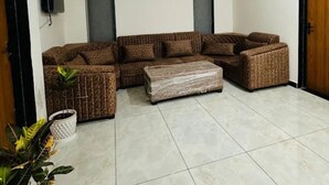 Uma sala de estar com sofá seccional, uma mesa de centro e uma televisão fixada na parede.