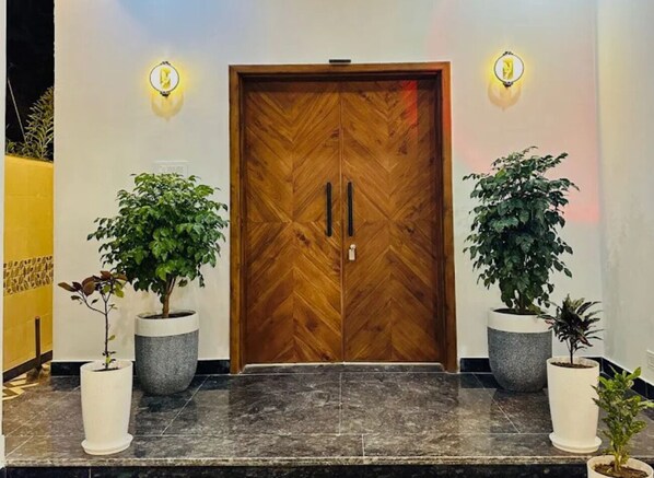 Dos puertas de madera dobles con un diseño de espiga, flanqueadas por dos macetas y dos lámparas fijadas a la pared.