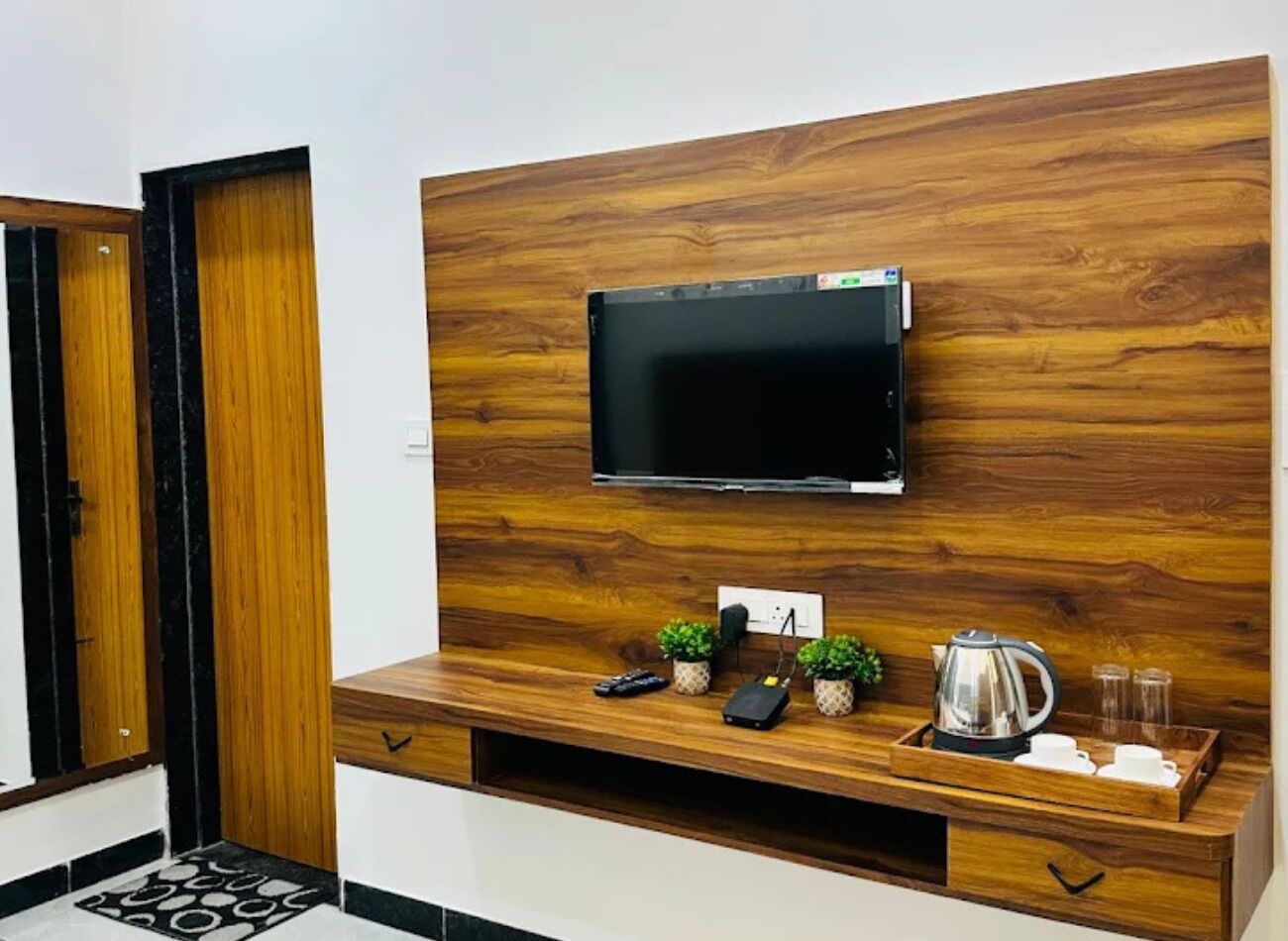 A modern living space with a flat-screen TV mounted on a wooden wall, a coffee table with a kettle, cups, and a remote control.