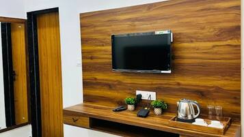 A modern living space with a flat-screen TV mounted on a wooden wall, a coffee table with a kettle, cups, and a remote control.
