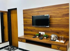 A modern living space with a flat-screen TV mounted on a wooden wall, a coffee table with a kettle, cups, and a remote control.