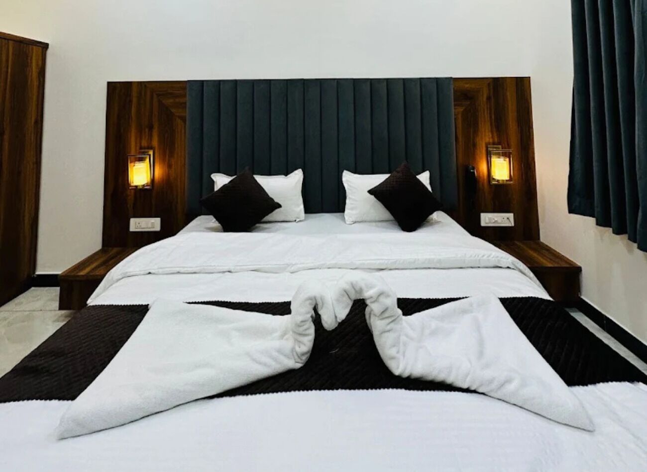 A neatly made bed with a dark headboard, white bedding, and black pillows.