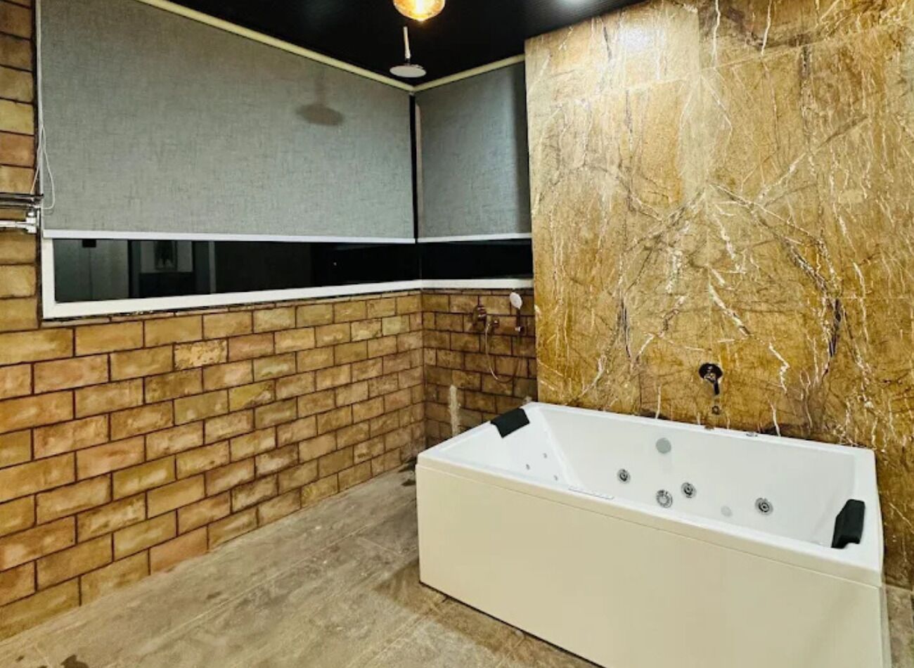 A modern bathroom with a brick wall, a large window, and a white bathtub.