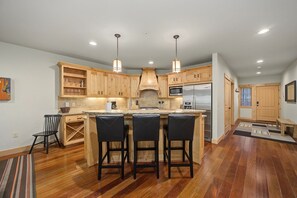A modern kitchen with wooden cabinets, a stainless steel refrigerator, and a bar area with stools. - Barlow Pass Condo 201 at South Grand Lodge | Spacious 3BR, In-Room Soaking Tub & Mt. Hood Getaway (Government Camp)