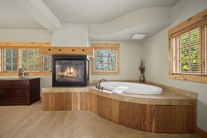 A bathroom with a built-in fireplace, a freestanding bathtub, and wooden paneling. - Barlow Pass Condo 201 at South Grand Lodge | Spacious 3BR, In-Room Soaking Tub & Mt. Hood Getaway (Government Camp)