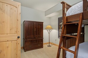 A bedroom with a bunk bed, wooden wardrobe, and a floor lamp. - Barlow Pass Condo 201 at South Grand Lodge | In-Room Soaking Tub (Government Camp)