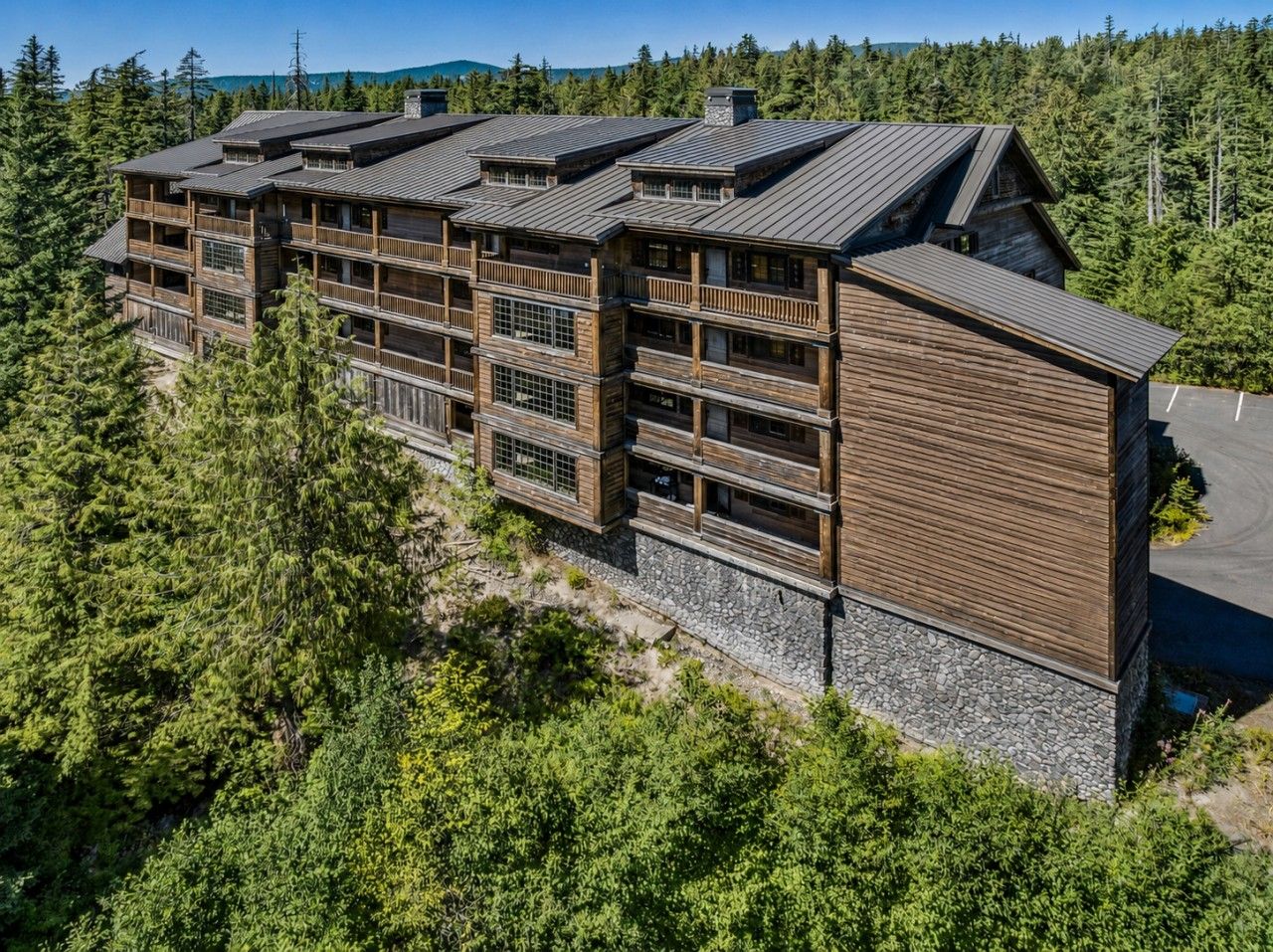 En fleretagers træbygning med balkoner, omgivet af tæt skov.