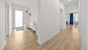 A modern, well-lit hallway with wooden flooring, a built-in laundry area, and a view into a room with a blue curtain. - Klimatizovaný apartmánový dom, vyhrievaný bazén (Dunajská Lužná)