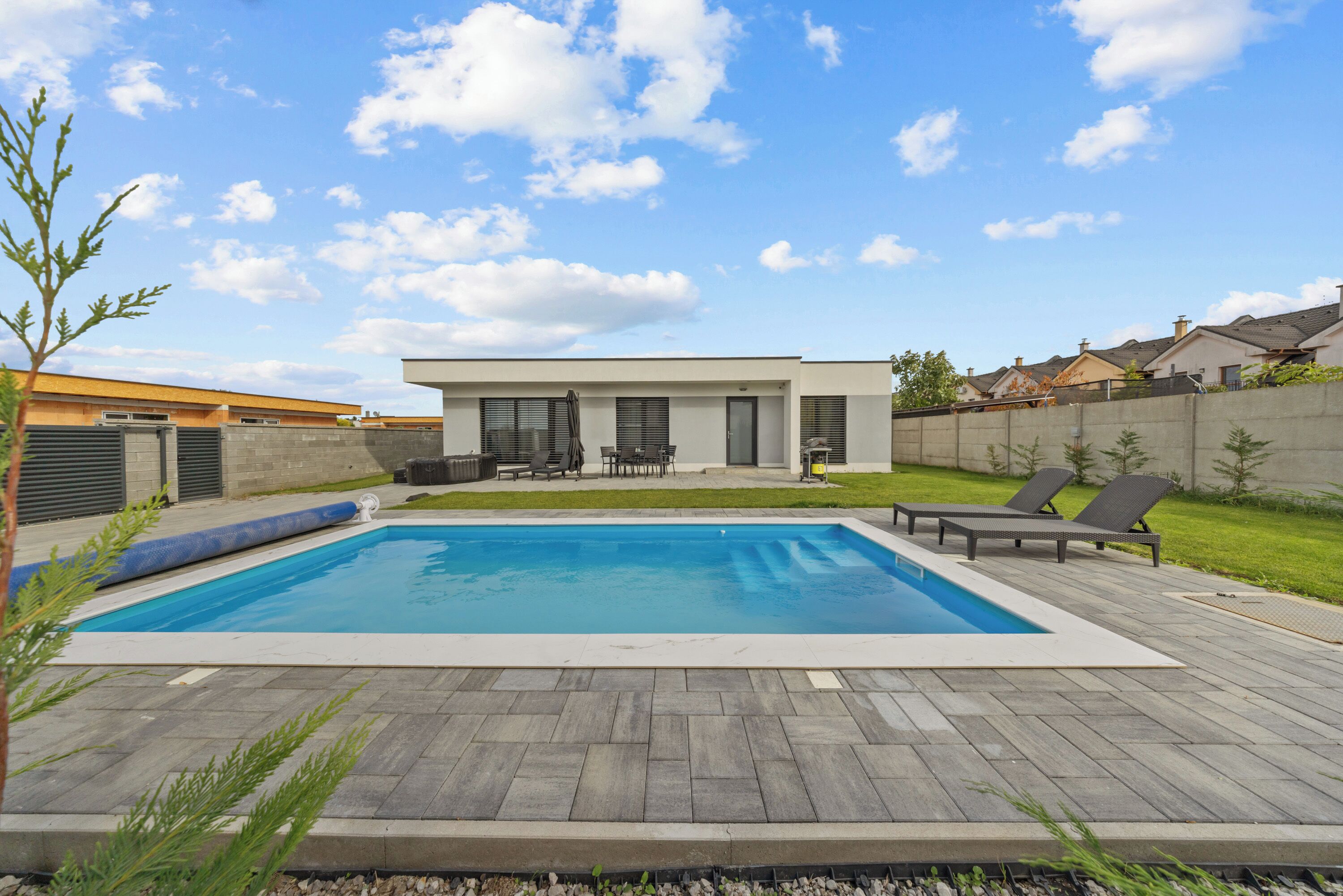 A rectangular swimming pool with a wooden deck, surrounded by a low wall and a grassy area.
