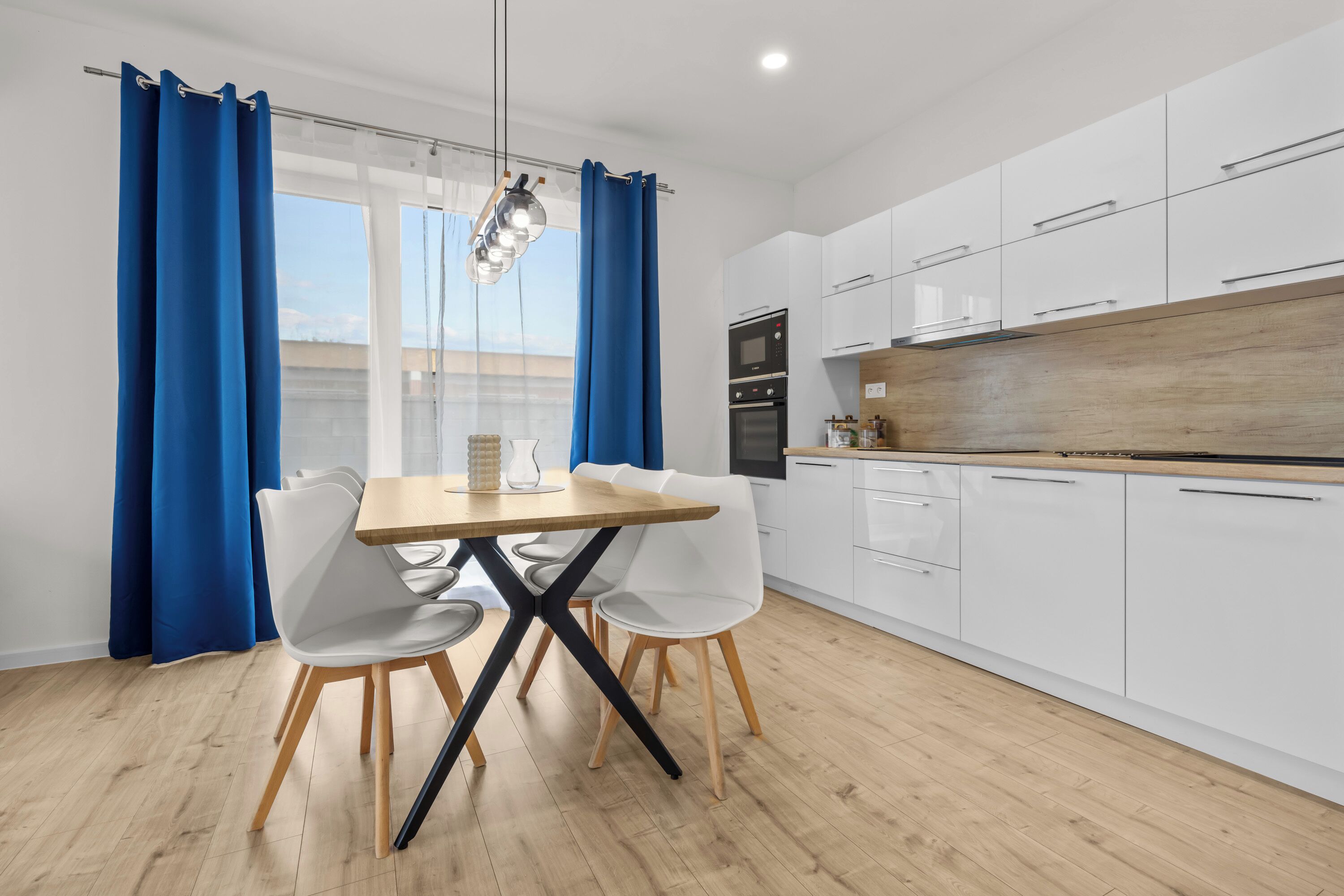 A modern kitchen with white cabinets, a wooden countertop, and a dining area with a table and chairs.