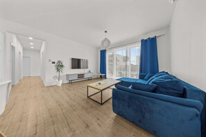 A modern living room with a blue sofa, a wooden coffee table, and a TV on a white console. - Klimatizovaný apartmánový dom, vyhrievaný bazén (Dunajská Lužná)