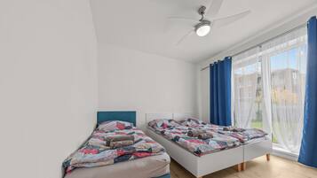 A modern bedroom with two single beds, a ceiling fan, and a large window with blue curtains.