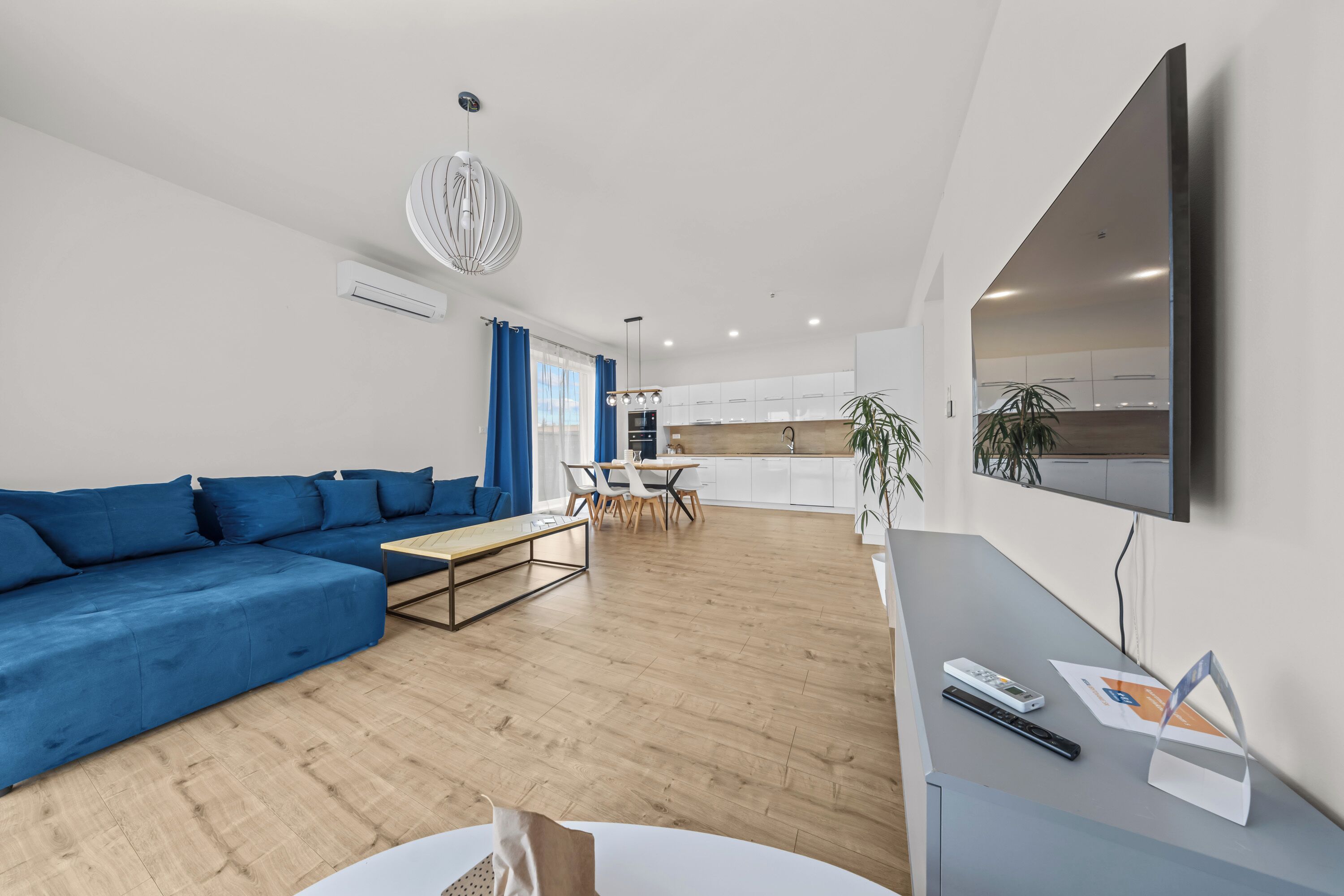 Un salon moderne avec un canapé bleu, un coin repas et une cuisine en arrière-plan.
