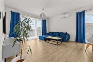 Ein modernes Wohnzimmer mit einem blauen Sofa, einem Holztisch und einer Topfpflanze.