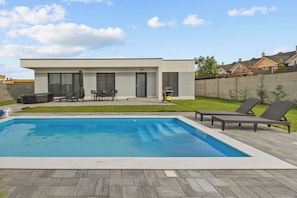 A modern house with a swimming pool, outdoor furniture, and a well-maintained lawn.