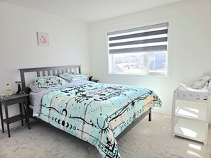 Un dormitorio con cama, mesitas de noche, una ventana con persianas y una cama litera.
