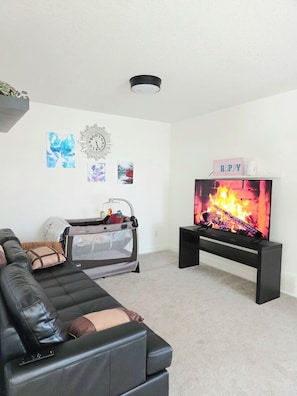 A living room with a black leather sofa, a television on a black stand, and a baby playpen. - Modern Luxury Home. High Cilings Near Airport. Netflix, Prime, Disney (Leduc)