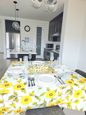 A dining area with a table set for four, featuring a sunflower tablecloth. - Modern Luxury Home. High Cilings Near Airport. Netflix, Prime, Disney (Leduc)