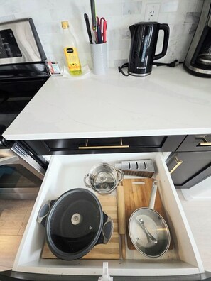 A kitchen with a white countertop, a black kettle, and a drawer containing pots and a wooden cutting board. - Modern Luxury Home. High Cilings Near Airport. Netflix, Prime, Disney (Leduc)