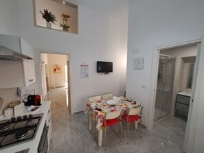 A compact kitchen with a stove, a dining table with chairs, a TV mounted on the wall, and a shower area. - A fully furnished apartment, perfect for relaxing in Puglia (Molfetta)
