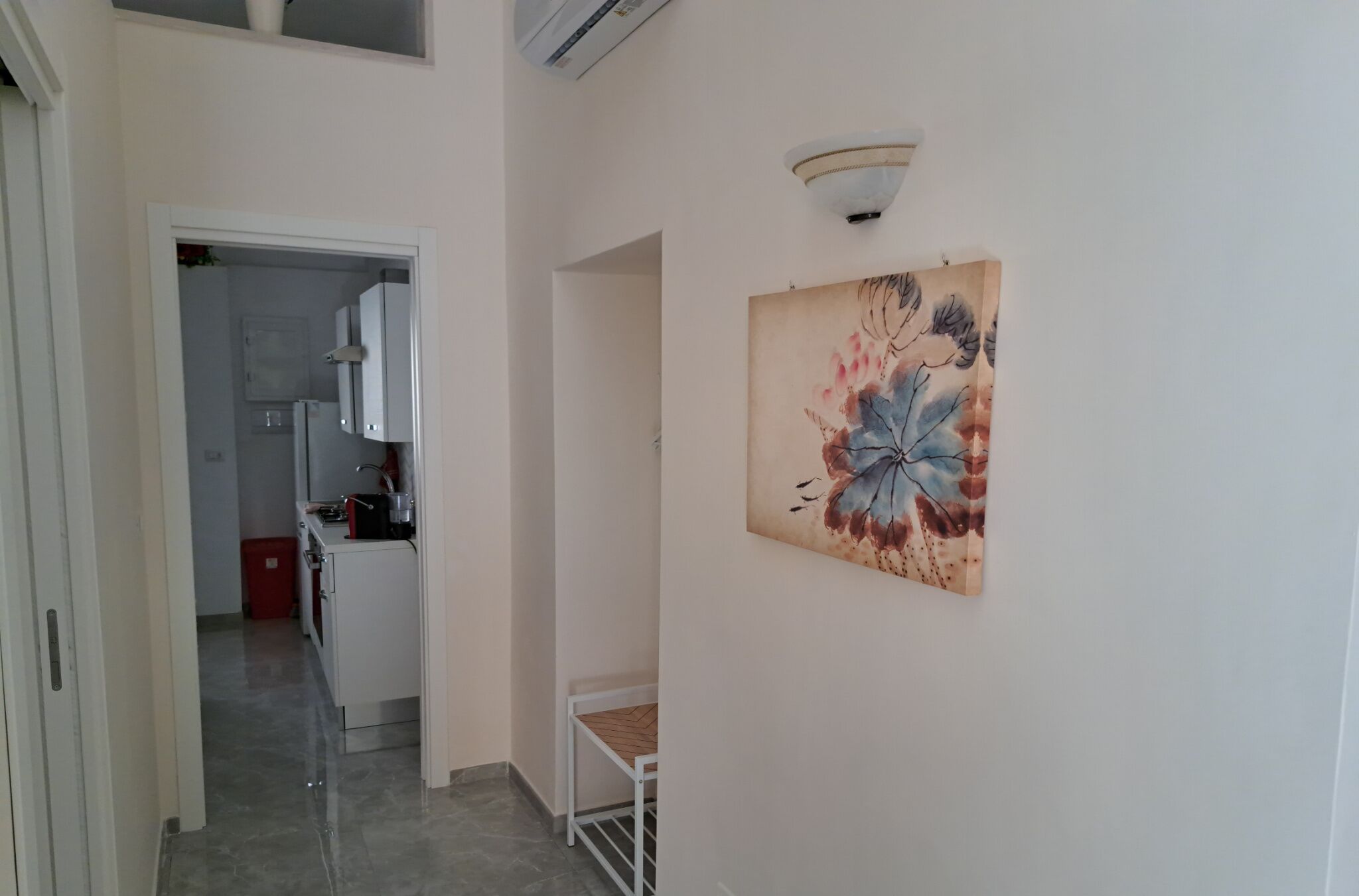 A hallway with a kitchen area visible through an open door, a small table, and a wall-mounted artwork.