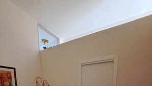 Een slaapkamer met een bed, een deur, een dressoir, een wandlamp en een lijst met een afbeelding.