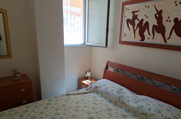 Une chambre à coucher comprenant un lit, une table de chevet, une commode, une fenêtre et un tableau accroché au mur.