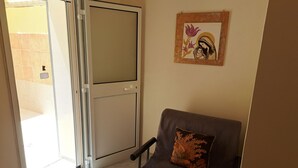 Een kamer met een schuifdeur naar een balkon, een grijze bank met een decoratief kussen, en een kunstwerk in een lijst aan de muur.