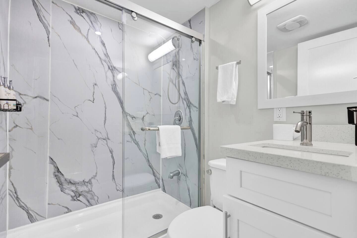 A modern bathroom with a glass-enclosed shower, a white toilet, and a marble-tiled wall.
