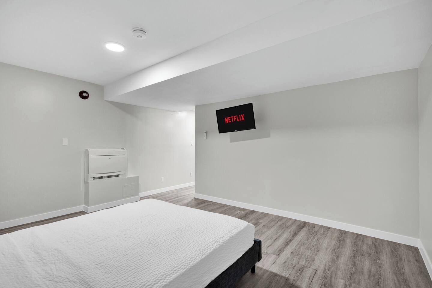 A bedroom with a bed, a wall-mounted TV, a ceiling light, and a wall-mounted air conditioner.