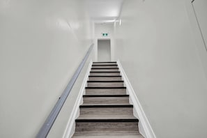 Eine Treppe mit Holzbodenstufen und einem Metallgeländer, die zu einer Tür mit einem Notausgangsschild führt.