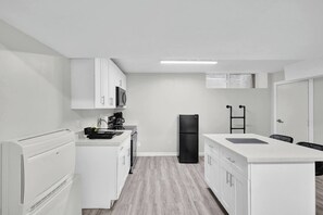 Cocina compacta con armarios blancos, refrigerador negro y microondas.