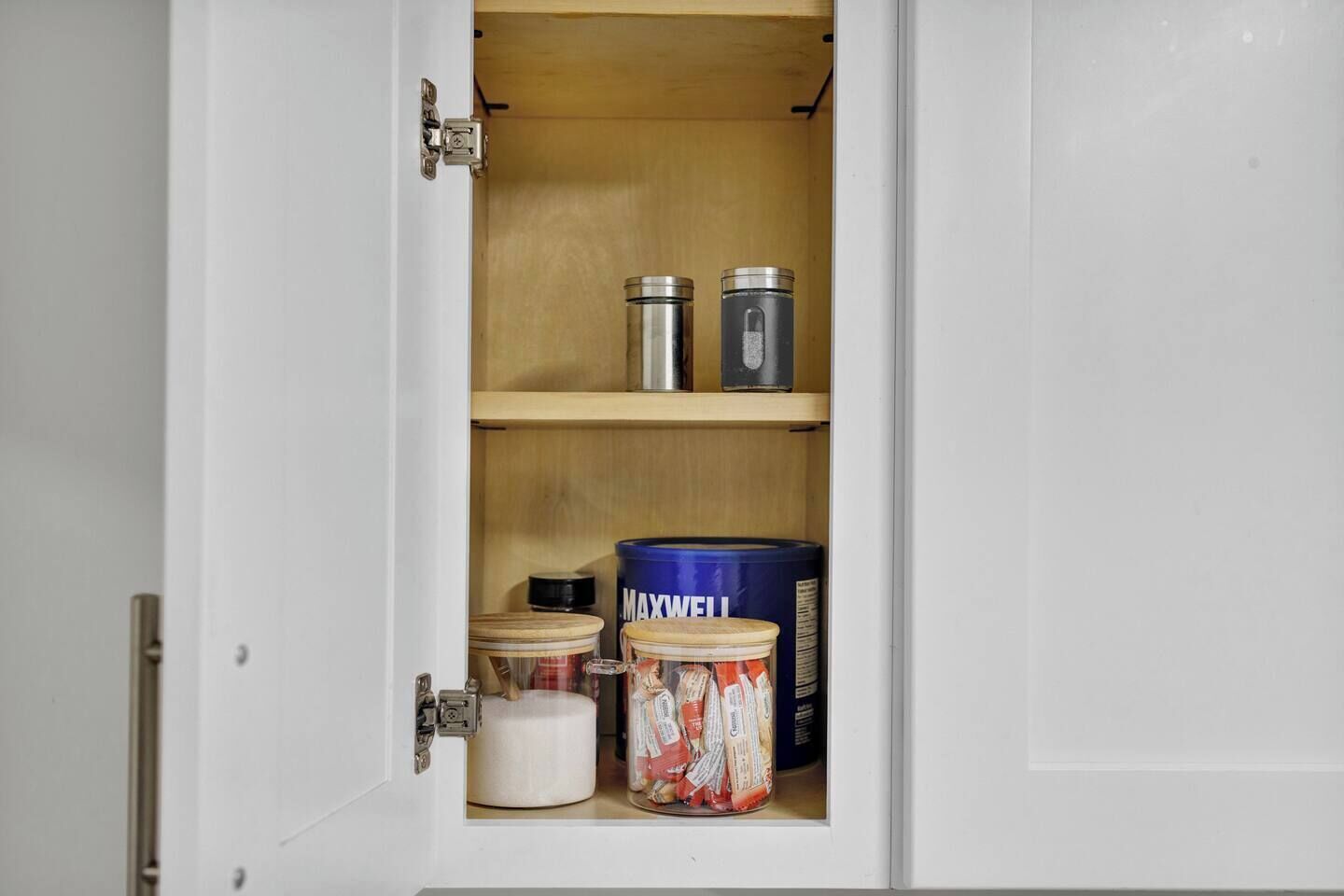 A cabinet with shelves containing various containers, including a blue can labeled 'MAXWELL' and a white cylindrical container.