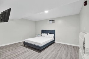Ein Schlafzimmer mit einem Bett, einem Nachttisch, einem an der Wand montierten Fernseher und einer Deckenleuchte.