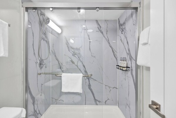 A modern bathroom with a glass-enclosed shower, marble walls, and a white bathtub.